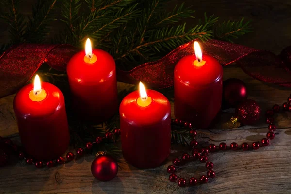 Cuatro velas rojas ardientes en el cuarto advenimiento, decoración de Navidad con ramitas de abeto y adornos en una mesa de madera rústica —  Fotos de Stock