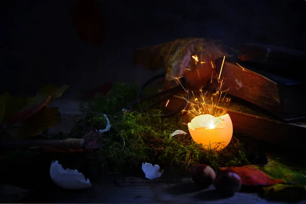 Gloeiende en sprankelende "eggshell" op mos met herfstbladeren en oude boeken, mysterieuze halloween stilleven tegen een donkere rustieke achtergrond — Stockfoto