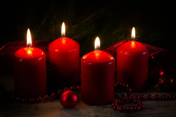 Four red burning candles at the fourth advent, christmas decoration with spruce twigs and baubles on a rustic board, dark background — Stock Photo, Image
