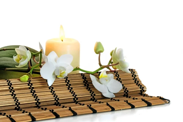 Combinación de spa con flores de orquídea, vela aromática ardiente y una estera antibalas aislada contra el blanco como fondo de esquina —  Fotos de Stock