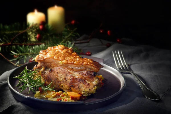 Pasto di maiale arrosto festivo con crosta croccante su un piatto grigio, tovaglia, decorazione natalizia e candele su uno sfondo scuro con spazio per la copia — Foto Stock
