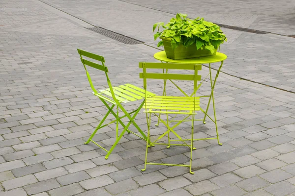 Sillas de jardín verde claro y una mesa plegable con una caja de flores verde en el mercado empedrado gris, concepto de arte, color en el desierto de hormigón de la ciudad urbana, espacio de copia — Foto de Stock