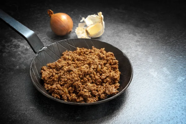 Fried ground beef with onion and garlic in a black pan on a dark stone background with copy space — Stock Photo, Image
