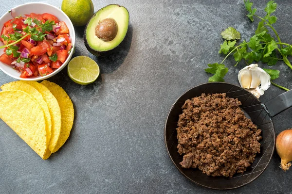 Taco összetevők sült marhahús, paradicsomos salsa, avokádó és gyógynövények háttéren sötét kő, másol hely, felülnézet, felülről — Stock Fotó