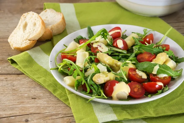 Ensalada de espárragos blancos, tomates cóctel y rúcula con salsa de ajo, servilleta verde en una mesa de madera rústica — Foto de Stock