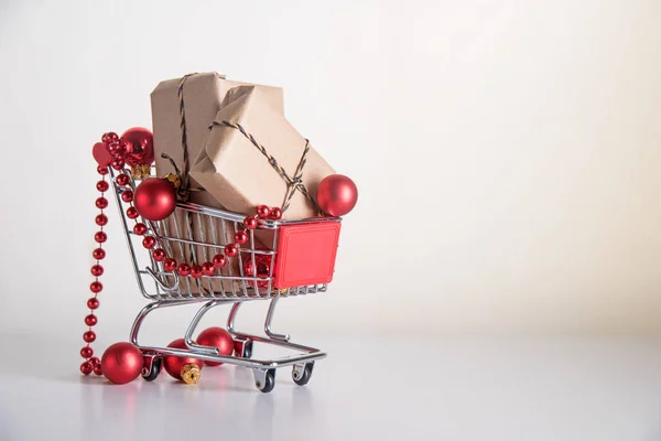 Christmas shopping, presentaskar i kraftpapper och röda julgranskulor i en kundvagn eller vagn på en ljus bakgrund med kopia utrymme — Stockfoto