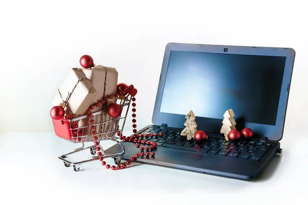 Online vásárlás karácsonyi baubles, és ajándék dobozok egy kosár vezetői közül egy laptop, a világos háttér-val másol hely — Stock Fotó