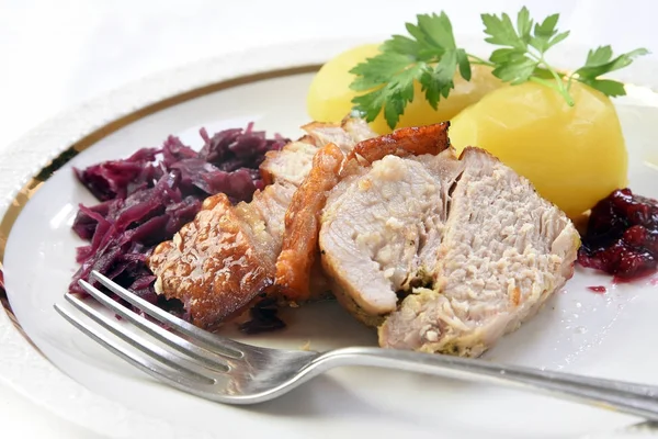 Жареная свинина с картошкой, красной капустой и клюквой на белой тарелке с вилкой — стоковое фото