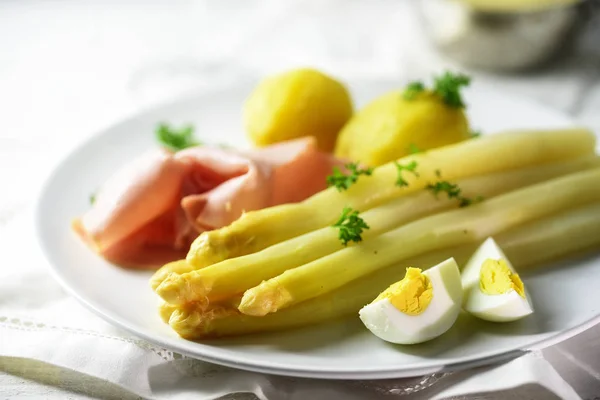 Белое блюдо из спаржи с картошкой, ветчиной и яйцом на белой тарелке, яркий фон, крупный план — стоковое фото