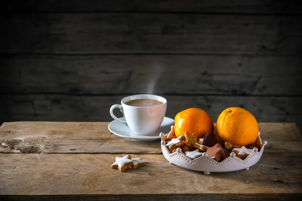 Christmas cookies and oranges in a bowl and a cup with hot coffee on a rustic table, dark wooden background with a large copy space — Stock Photo, Image