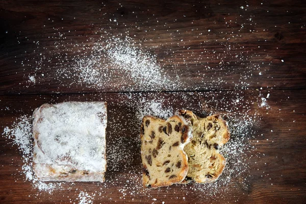 Sfondo di Natale, torta criststollen tedesco cosparso di zucchero a velo su una scura tavola di legno rustico, vista dall'alto, spazio copia — Foto Stock