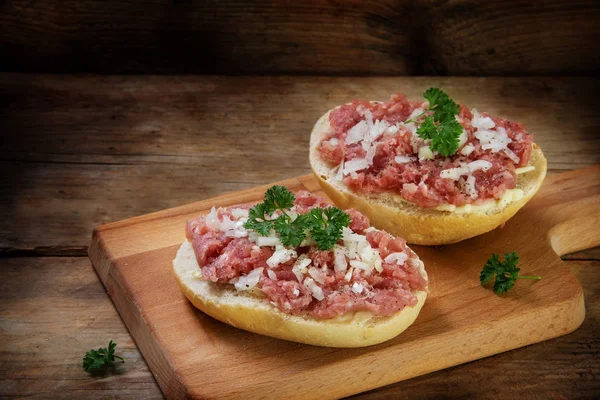 German mettwurst brotzeit, minced pork sausage with onions and parsley garnish on buns, cutting board on a dark rustic wooden background, copy space — Stock Photo, Image