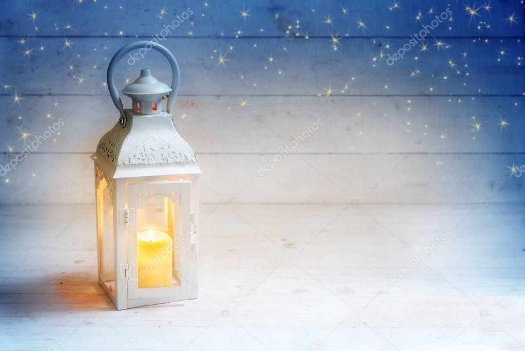 Christmas background with a lantern and burning candle light on rustic white wood, blue sky with stars, copy space 