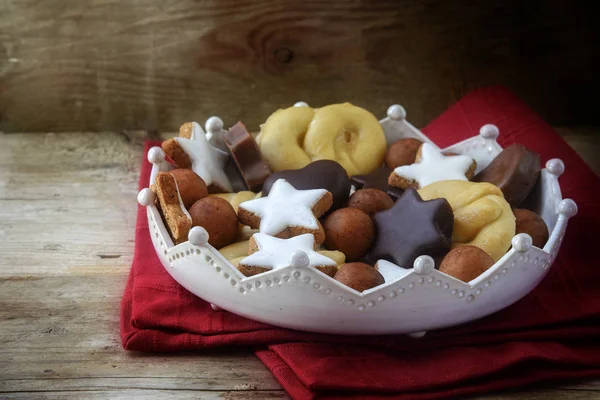 Biscuits de Noël et bonbons comme les étoiles de cannelle maison, boules de massepain, chocolat et biscuit dans un bol de couronne de poterie sur une serviette rouge, fond en bois rustique, espace de copie — Photo