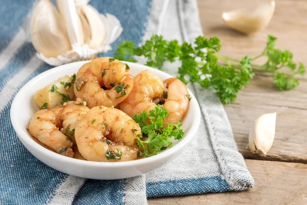 Shrimps or prawns and garlic in olive oil with parsley garnish in a white bowl, blue napkin on a rustic wooden table, spanish tapas appetizer gambas al ajillo — Stock Photo, Image
