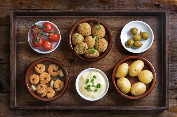 Spanish tapas such as baked olives, prawn shrimps, potatoes, tomato and garlic dip, party  appetizers on a rustic wooden tray, flat top view from above — Stock Photo, Image