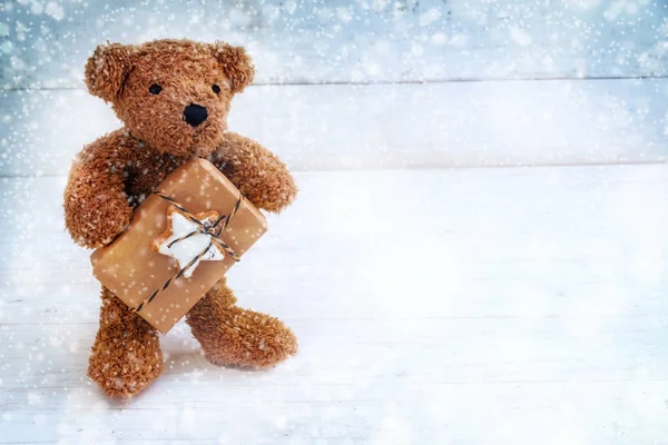 Osito de peluche con un regalo de Navidad de pie sobre un fondo de madera pintado de azul blanco en la nieve, espacio para copiar —  Fotos de Stock