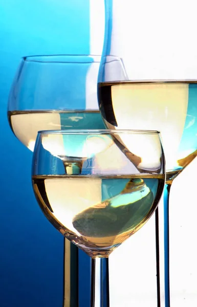 Αφηρημένη closeup, τρία ποτήρια κρασιού με λευκό κρασί μπροστά από ένα μπλε λευκό φόντο — Φωτογραφία Αρχείου