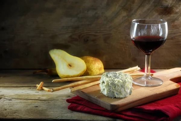 Creamy blue stilton cheese, port wine, pears and some cracker sticks on a cutting board and a red napkin against a dark rustic wooden background, copy space — Stock Photo, Image