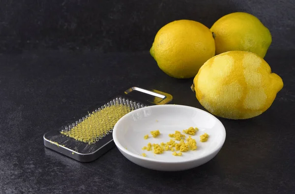 Fruta de limón orgánica, cáscara o corteza recién rallada y el rallador de metal sobre un fondo de pizarra oscura con espacio para copiar — Foto de Stock