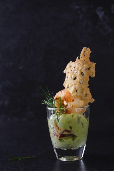 Crema de aguacate guacamole con camarones tigre o gambas y galleta de queso en un vaso, aperitivo o merienda de fiesta sobre un fondo de pizarra oscura con espacio para copiar — Foto de Stock