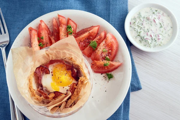 Muffin aux œufs et bacon dans du pain grillé, petit déjeuner de Pâques créatif avec tomates et trempette au fromage, vue du dessus, serviette bleue, table en bois peint en blanc — Photo