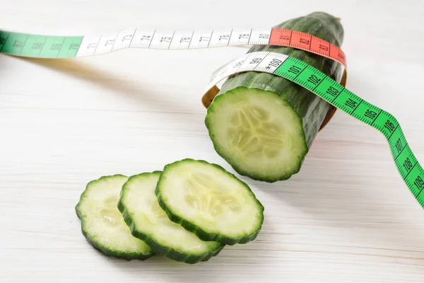 Pepino fresco y una cinta métrica sobre un fondo de madera blanca, concepto de alimentación saludable y dieta adelgazante — Foto de Stock