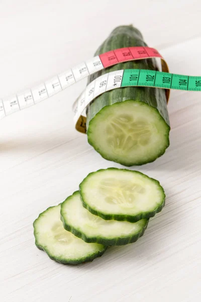 Pepino fresco y una cinta métrica sobre un fondo de madera blanca, concepto de alimentación saludable y dieta adelgazante — Foto de Stock