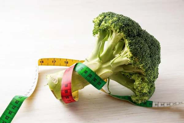 Brócoli fresco y una cinta métrica sobre un fondo de madera blanca, concepto de alimentación saludable y dieta para adelgazar con verduras, espacio para copiar — Foto de Stock