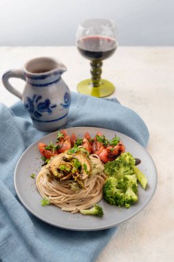 Bütün chamignons, brokoli, domates ve bitki garnitür spagetti tahıl, rustik taş masa lambası, şarap sürahisi peçeteye mavi ve arka planda cam, uzay, dikey kopyalama