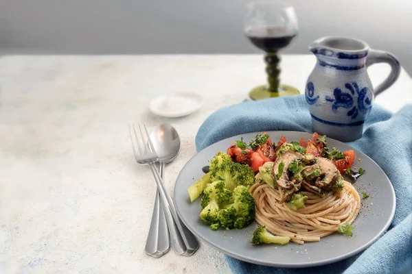 Fullkorn spagetti med chamignons, broccoli och tomater, blå servett på en rustik ljusbord, vin kanna och glas i bakgrunden, kopia utrymme — Stockfoto