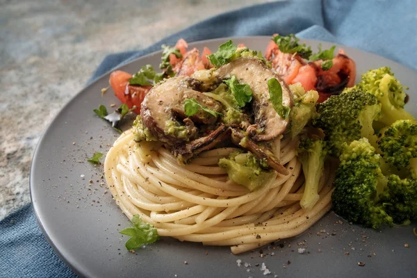 Цельнозерновые спагетти с шампиньонами, брокколи и помидорами, голубая салфетка на деревенском камне — стоковое фото