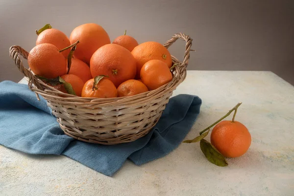 Корзина со свежими апельсиновыми фруктами и клементинами с листьями на голубой салфетке, серый деревенский фон с копировальным пространством — стоковое фото