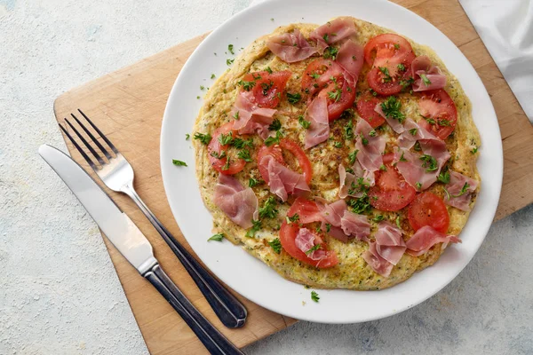 Omelette aux tomates, jambon de prosciutto et persil garnissent sur une planche de cuisine, fond gris clair, vue grand angle d'en haut, espace à copier — Photo