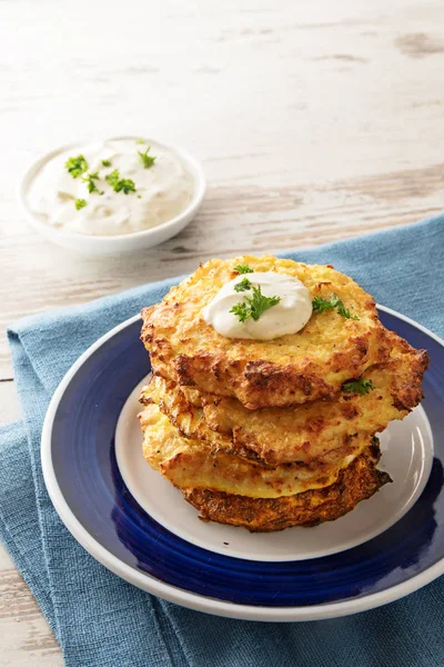 Pila dorata di rosti fritti di cavolfiore e parmigiano con un tuffo cremoso e guarnitura di prezzemolo, tovagliolo blu, tavolo in legno luminoso con spazio copia, verticale — Foto Stock