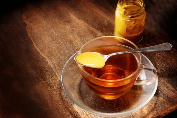 Μαύρο τσάι σε ένα γυάλινο Κύπελλο και ένα κουτάλι με μέλι σε ρουστίκ σκούρο ξύλο, υγιείς ζεστό ρόφημα με κρύο και τη γρίπη, αντίγραφο χώρου — Φωτογραφία Αρχείου