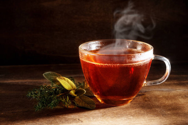 tea freshly brewed in a glass cup and some herbs on a dark rustic wooden background, healthy hot drink against cold and flu, copy space