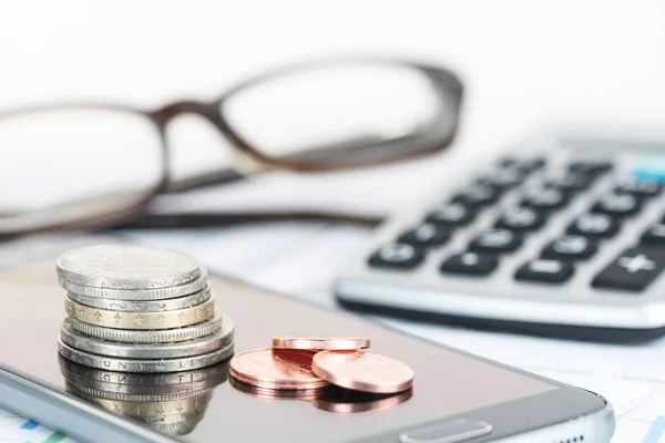 Pila de monedas en un teléfono, calcualtor y gafas borrosas en el fondo, concepto de finanzas para las empresas, la economía, la pensión y la pobreza, de cerca con enfoque seleccionado —  Fotos de Stock