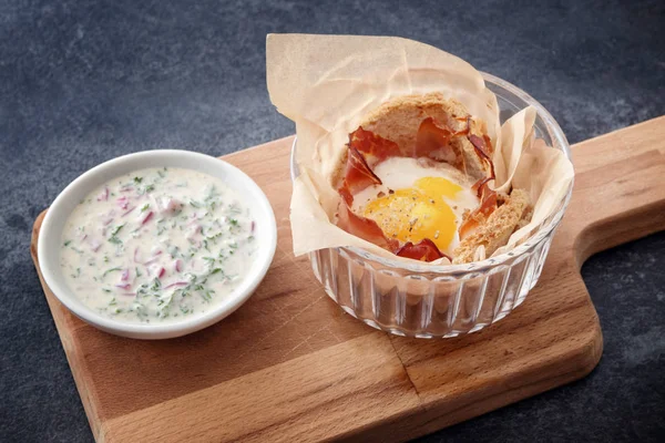 Magdalena de huevo con tocino y pan tostado y una salsa de queso fresco con hierbas en una tabla de cortar de madera, fondo de pizarra oscura — Foto de Stock