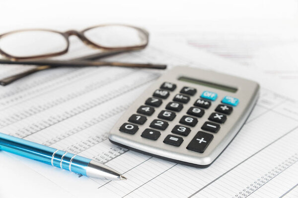 calculator, pen and glasses on a printed financial report with number tables, business concept for finance, economy and taxes