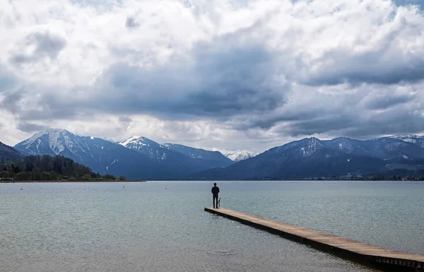 Joven parado solo en el embarcadero en el lago Tegernsee y mirando las montañas azules en el famoso complejo turístico de los Alpes bávaros, Baviera, Alemania, Europa — Foto de Stock