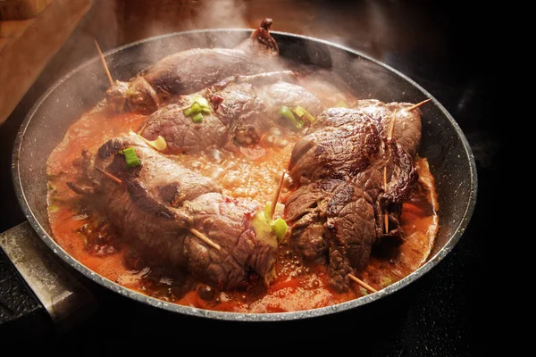 Memasak daging sapi roulades, Jerman diisi daging gulung dengan sayuran dan saus mengepul dalam panci di atas kompor hitam — Stok Foto