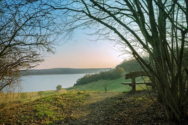 Banco de madera en una colina con vistas al río trave en la luz de la mañana, paisaje en primavera cerca de Luebeck en el Mar Báltico en Alemania, espacio de copia — Foto de Stock