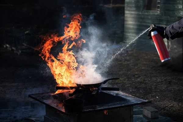 Muž hašení ohně na rozpálené litinové pánvi s pěnou ze spreje mohou, demonstrace během hasiči školení, tmavé pozadí s kopií prostor — Stock fotografie