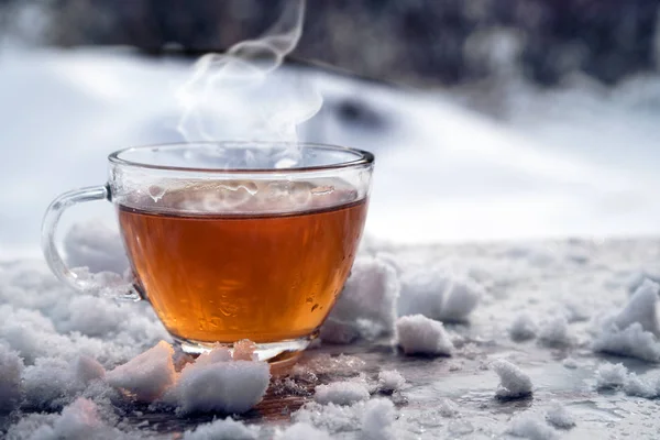 Chá quente fumegante em uma xícara de vidro está de pé fora em um dia frio de inverno com neve, espaço de cópia — Fotografia de Stock