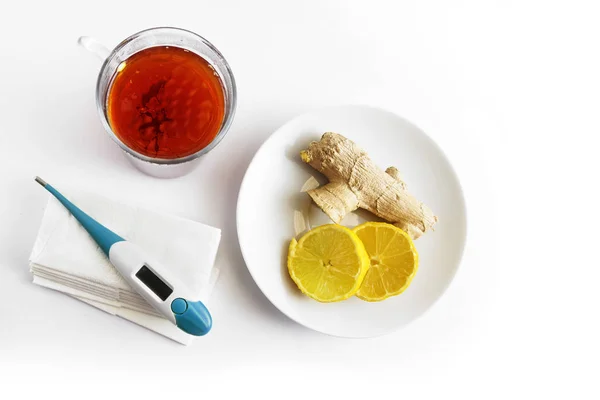 Heißer Tee, ein Teller mit Zitrone und Ingwer und ein medizinisches Thermometer auf Papiertaschentüchern, Gesundheitskonzept gegen Erkältung und Grippe auf hellem Hintergrund mit Kopierraum — Stockfoto