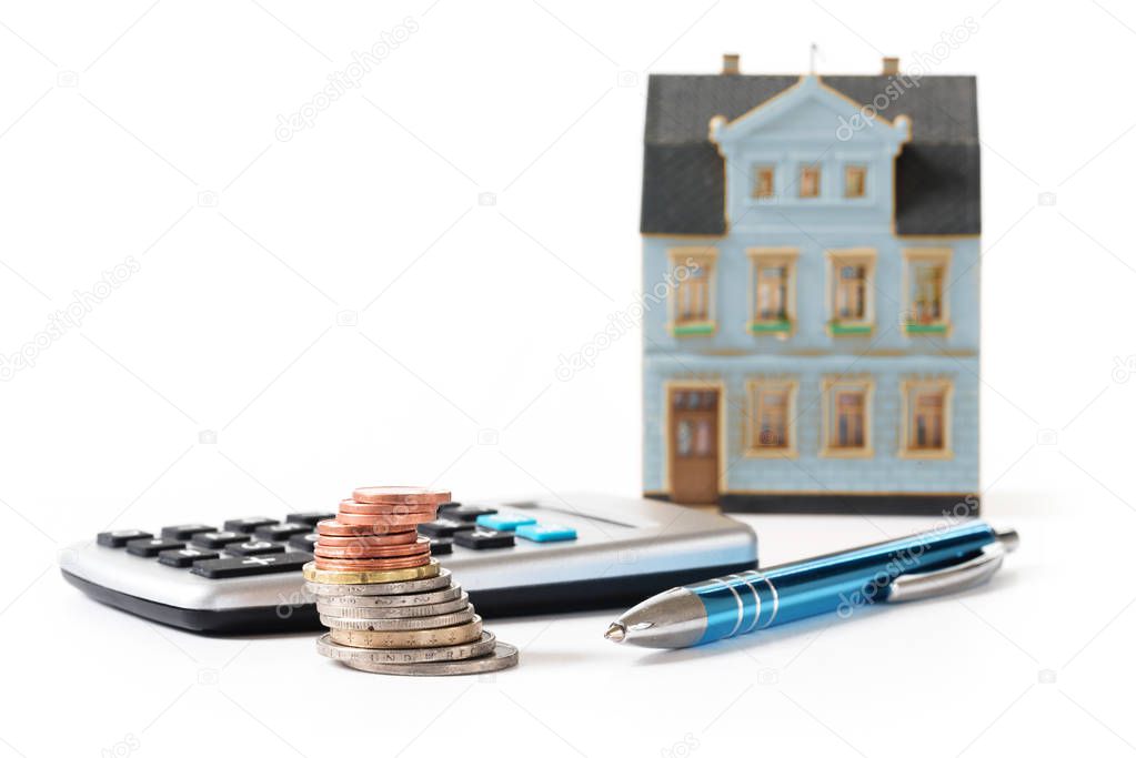 coins, calculator and pen in front of a blurred house model, calculation of the cost of a real estate investment or rent, isolated on a white background