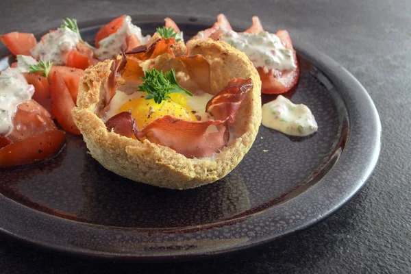 Μάφιν από το αυγό και μπέικον με φρυγανισμένο ψωμί, ντομάτες και τυρί κρέμα με μυρωδικά σε ένα σκοτεινό πιάτο σε ρουστίκ σχιστόλιθος, δημιουργικό πρωινό, Μπραντς ή σνακ, επιλεγμένα focus — Φωτογραφία Αρχείου