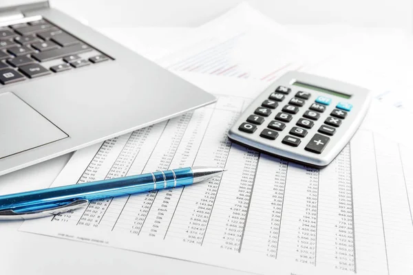 Pen, calculator and laptop lying on a financial report with number charts on the desk in the office, concept for business, finance and taxes, copy space Royalty Free Stock Images