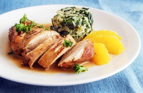 Petto di pollo con fette di arancia e riso agli spinaci su un piatto bianco, cena dietetica con poche calorie, tovaglia blu — Foto Stock